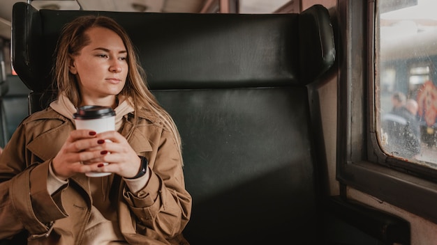 Frau, die im Zug sitzt und einen Kaffee hält
