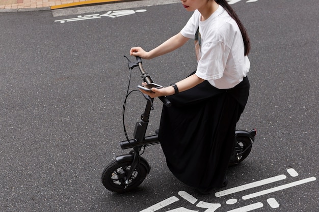 Kostenloses Foto frau, die in der stadt elektrofahrrad fährt und smartphone hält