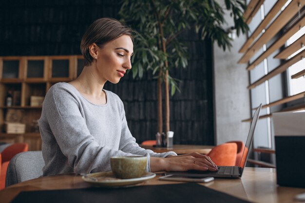 Frau, die in einem trinkenden Kaffee des Cafés sitzt und an einem Computer arbeitet