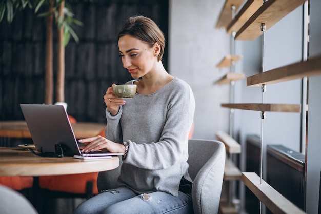 Frau, die in einem trinkenden Kaffee des Cafés sitzt und an einem Computer arbeitet