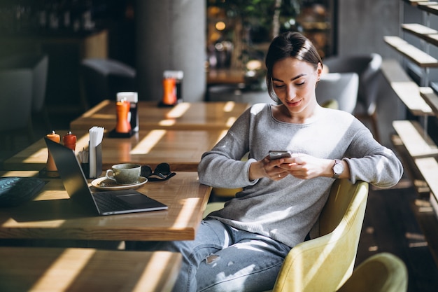 Kostenloses Foto frau, die in einem trinkenden kaffee des cafés sitzt und an einem computer arbeitet