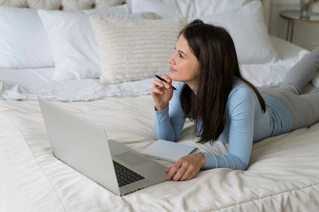 Frau, die in ihrem Bett bleibt, während sie einen Videoanruf auf ihrem Laptop hat