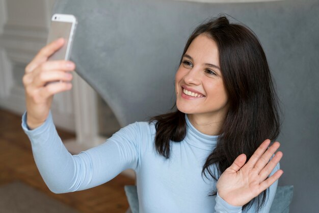 Frau, die in ihrem Bett bleibt, während sie einen Videoanruf auf ihrem Smartphone hat