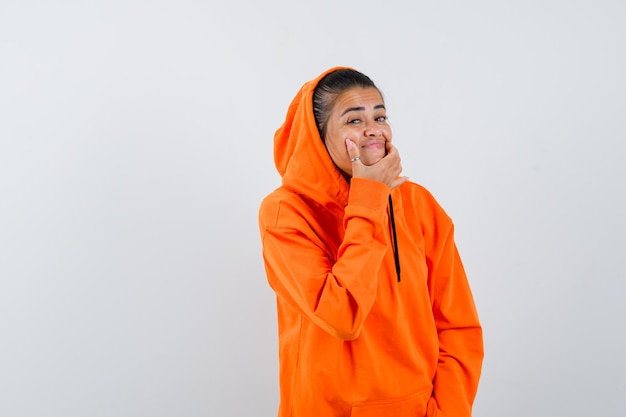 Frau, die in orangefarbenem Hoodie ein Lächeln auf dem Gesicht erzwingt und komisch aussieht