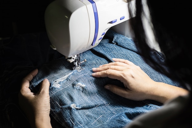 Frau, die Jeanspatchwork unter Verwendung der Nähmaschine - nähendes Konzept des Hauses DIY tut