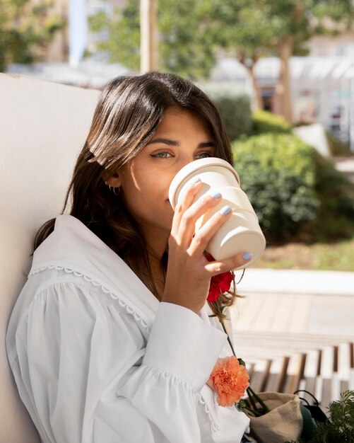 Frau, die Kaffee draußen beim Halten von Blumen hat