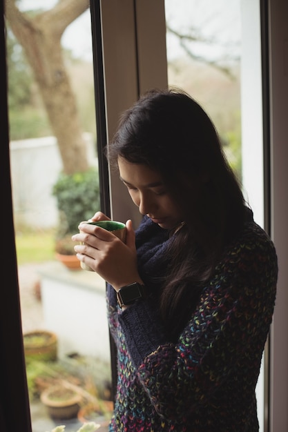 Frau, die kaffee nahe fenster zu hause hat