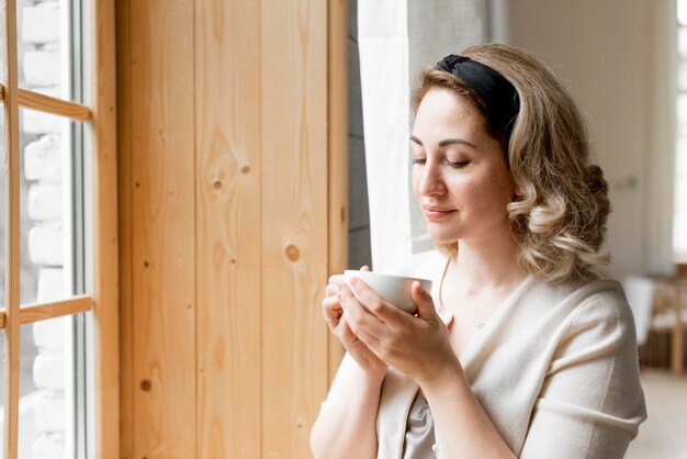 Frau, die Kaffee neben ihrem Fenster trinkt