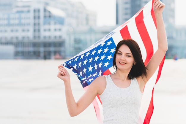 Kostenloses Foto frau, die kamera betrachtet und breite amerikanische flagge wellenartig bewegt