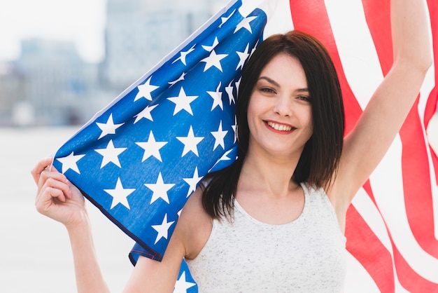 Kostenloses Foto frau, die kamera betrachtet und wellenartig bewegende breite amerikanische flagge lächelt