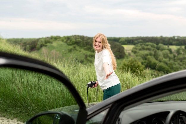 Kostenloses Foto frau, die kamera hält und vor auto aufwirft