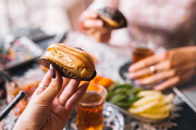 Frau, die Karamell-Eclair hält, diente für Tee-Einrichtung