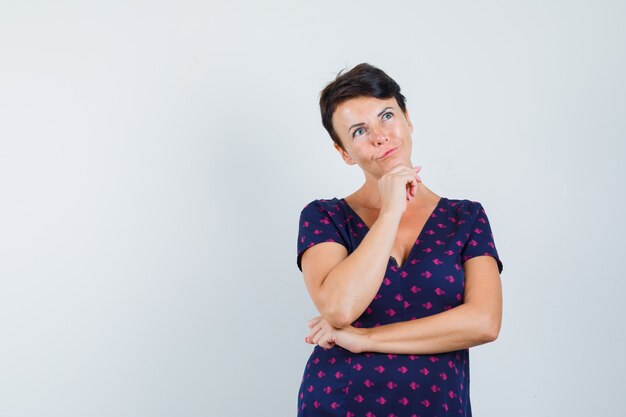 Frau, die Kinn auf Hand im Kleid stützt und unschlüssig schaut.