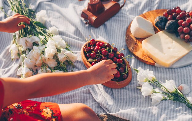 Frau, die Kirschen vom hölzernen Teller mit Blumen, Käse und Früchten aufnimmt