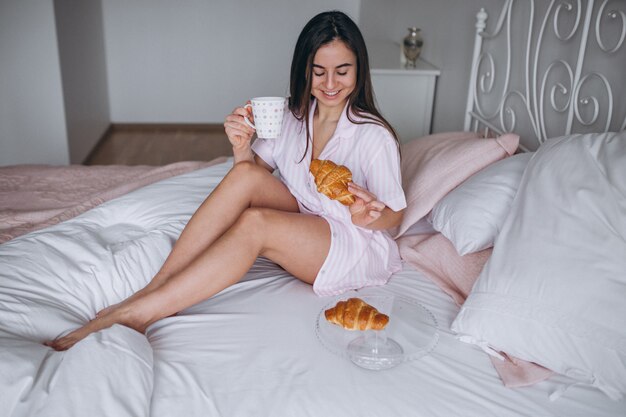 Frau, die köstliches Hörnchen mit Kaffee im Bett isst