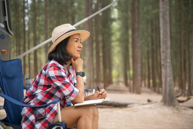 Frau, die Laptop nahe dem Campingplatz betrachtet. Wohnwagen Auto Urlaub. Familienurlaubsreise, Urlaubsreise im Wohnmobil. Frau liest ein Buch im Kofferraum. weibliches Lernen in der Reisepause, Legen