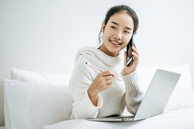 Frau, die Laptop spielt und am Telefon spricht.