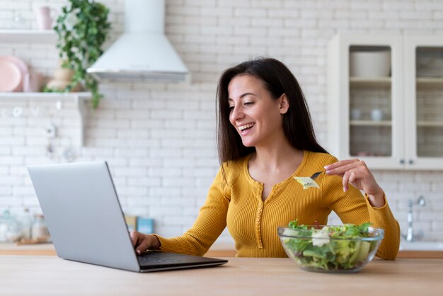 Frau, die Laptop überprüft und Salat isst