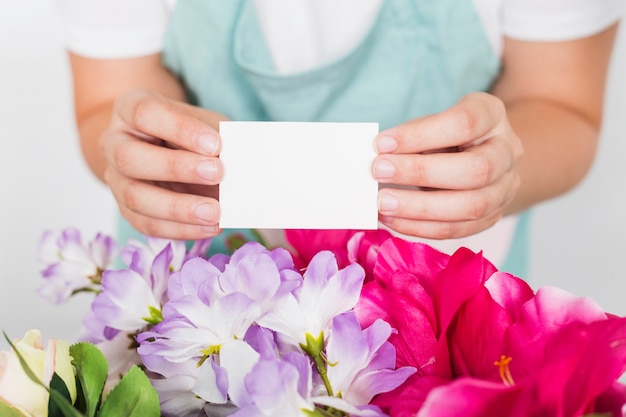 Frau, die leere Visitenkarte über frischen Blumen hält