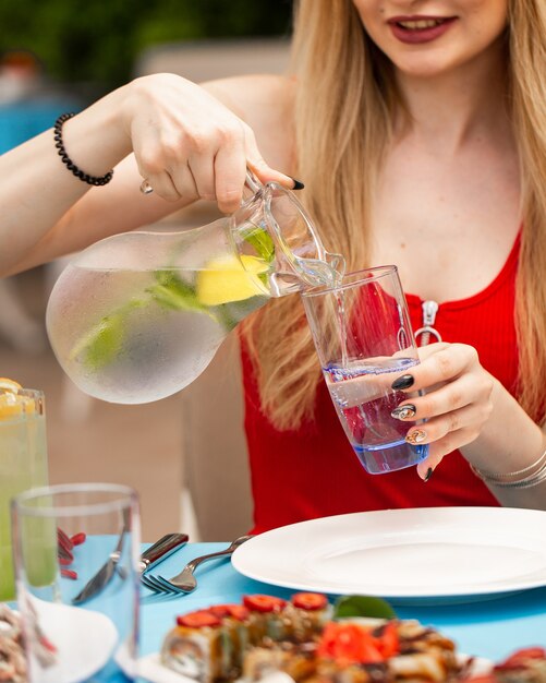 Frau, die Limonade vom Glas in Glas hinzufügt.