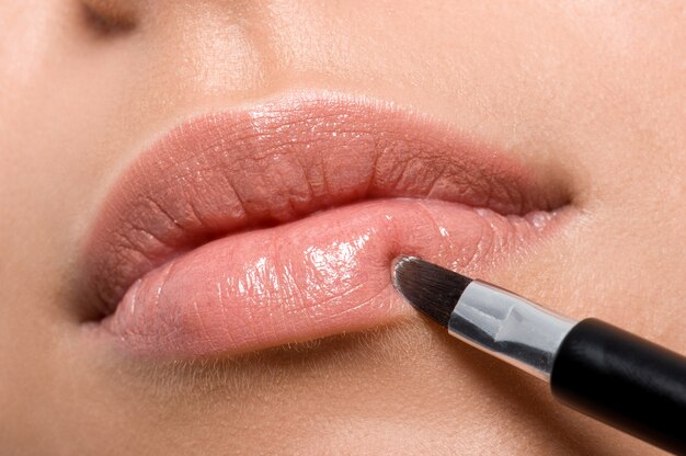 Frau, die Lippenstift auf Lippen mit Pinsel - Nahaufnahme anwendet