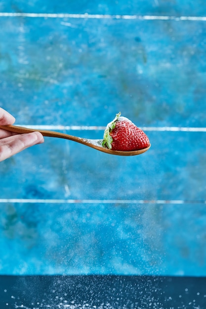 Frau, die Löffel Erdbeere auf blauer Oberfläche hält