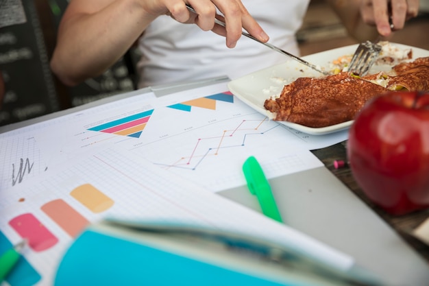 Frau, die Mahlzeit auf Tabelle nahe Grafiken und Diagrammen isst