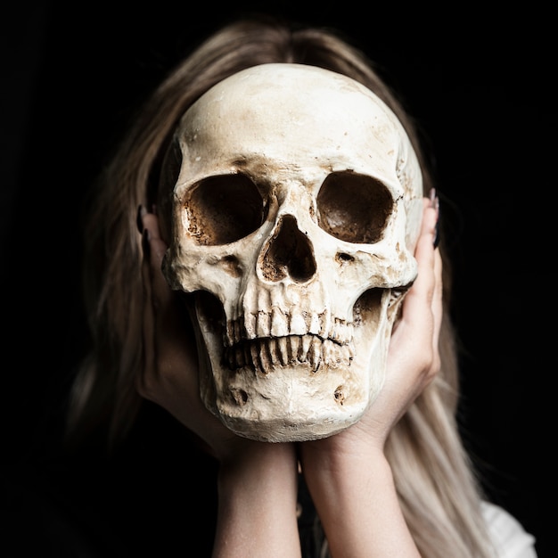 Frau, die menschlichen Schädel mit schwarzem Hintergrund hält