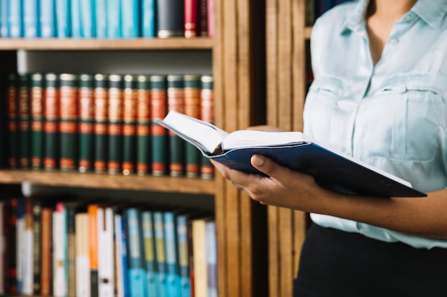 Frau, die mit Buch in der Bibliothek steht