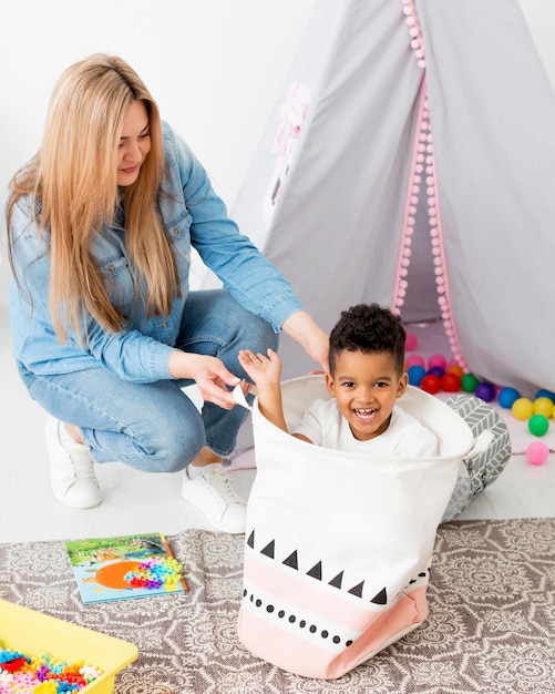 Frau, die mit dem Jungen im Korb zu Hause spielt