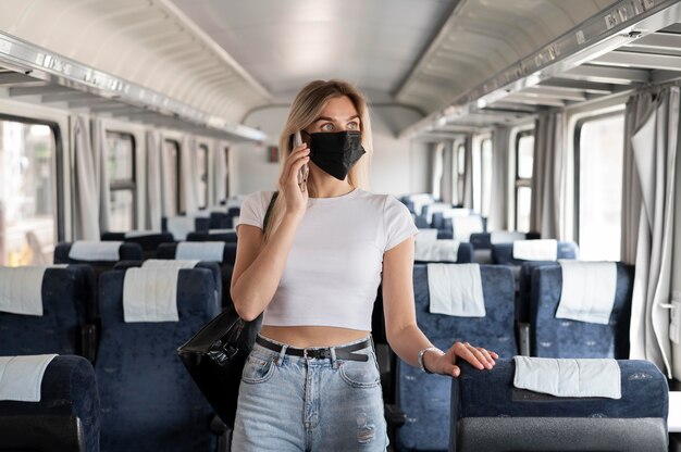 Frau, die mit dem Zug reist und telefoniert, während sie eine medizinische Maske trägt