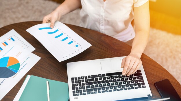 Frau, die mit Finanzdiagrammen auf dem Tisch arbeitet. Laptop, Papiere