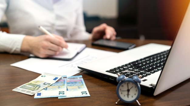 Frau, die mit Finanzen auf dem Tisch arbeitet. Laptop, Smartphone, Geld, Notizblock, Uhr