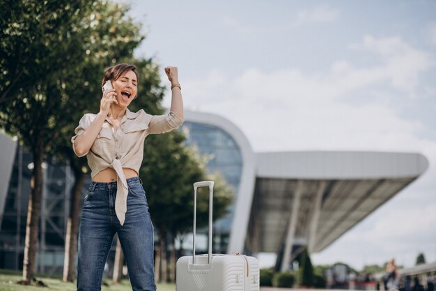 Frau, die mit Gepäck am Flughafen reist und telefoniert