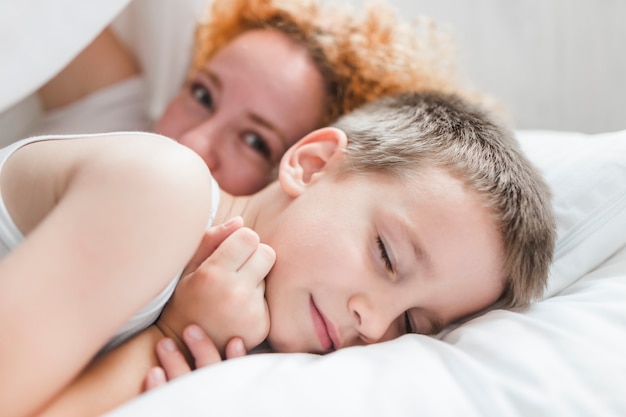 Frau, die mit ihrem schlafenden Sohn auf Bett liegt