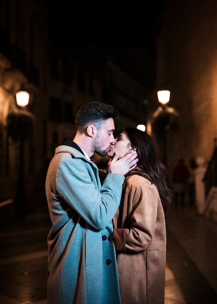 Frau, die mit jungem Mann auf Promenade nachts umfasst und küsst