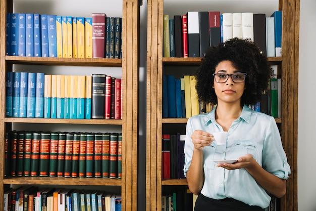 Frau, die mit Kaffeetasse in der Bibliothek steht