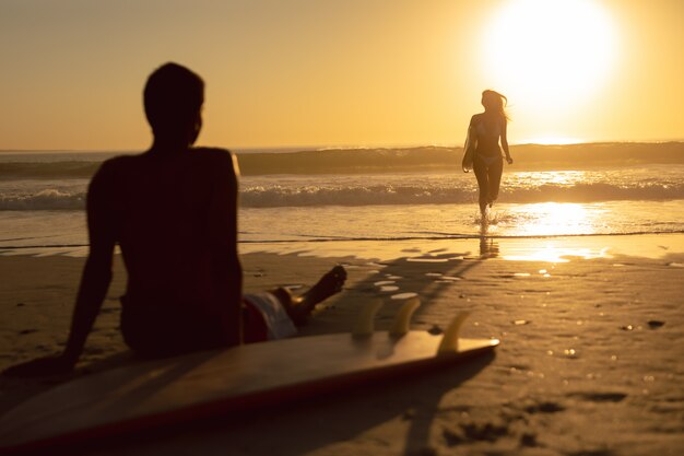 Frau, die mit Surfbrett während Mann sich entspannt auf dem Strand läuft