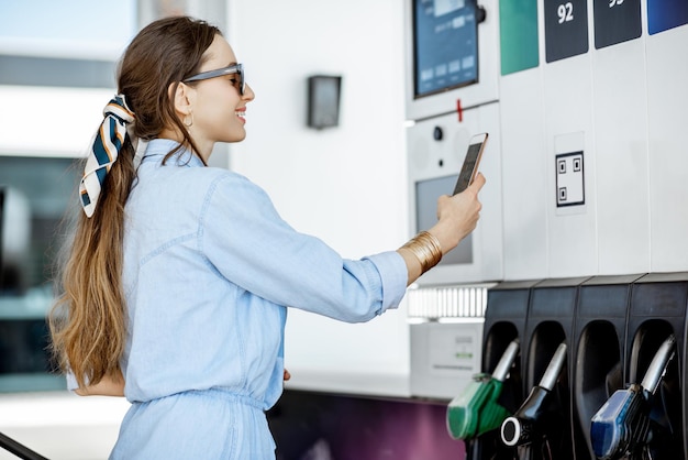 Frau, die mit telefon für benzin bezahlt, barcode an der tankstelle fotografieren