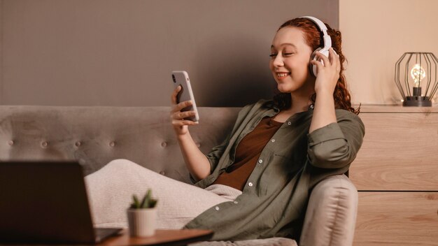 Frau, die moderne Kopfhörer und Smartphone auf dem Sofa zu Hause verwendet