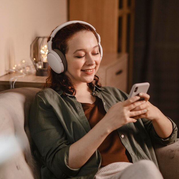 Frau, die moderne Kopfhörer und Smartphone-Gerät zu Hause verwendet