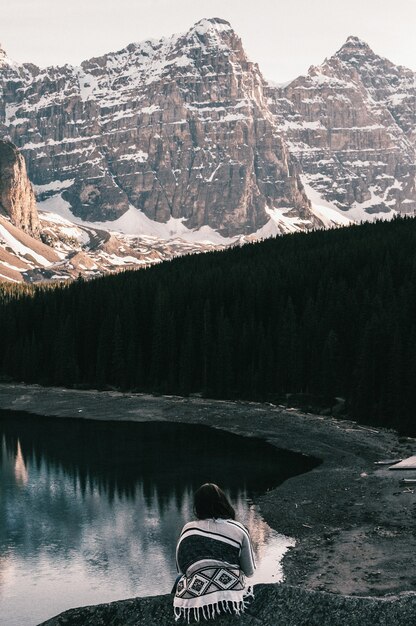 Frau, die nahe dem Moränensee sitzt und die schneebedeckten Berge bewundert