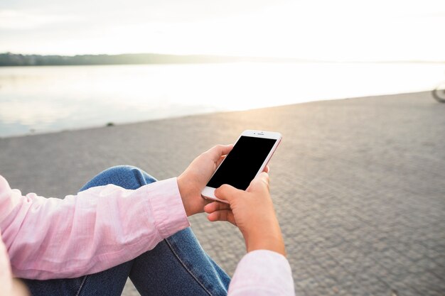 Frau, die nahe dem See unter Verwendung des Mobiltelefons sitzt