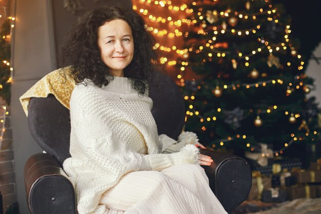 Frau, die nahe Kamin sitzt. Dame in einem weißen Pullover. Brünette in einem Weihnachtskonzept.