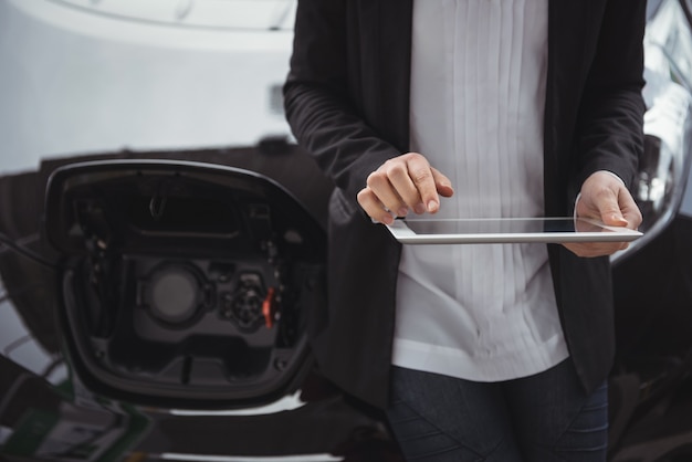 Frau, die neben elektroauto steht und digitales tablett verwendet