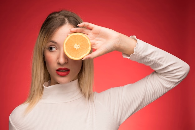 Frau, die orange Scheibe über ihrem Auge hält