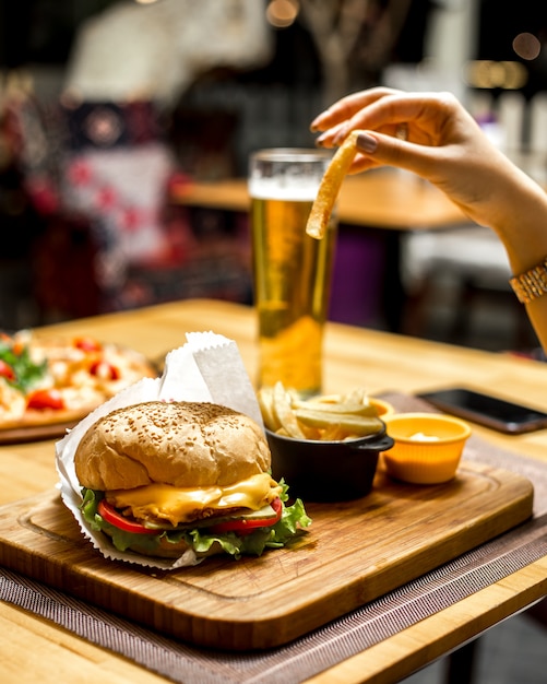 Frau, die pommes frites und sandwich mit käse und tomate und mit soße isst