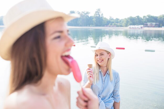 Frau, die Popsicle vor ihrem Freund hält Eiscremekegel nahe dem See leckt