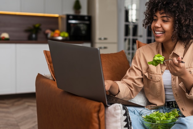Frau, die Salat isst und auf Laptop schaut