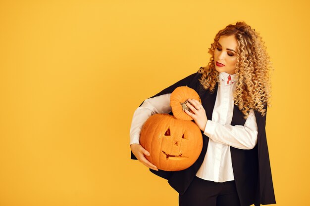 Frau, die schwarzes Kostüm trägt. Dame mit Halloween Make-up. Mädchen, das auf einem gelben Hintergrund steht.